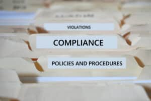 Compliance in the workplace concept - File folders marked Compliance Policies Regulations Violations Procedures and Documentation.
