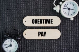 wage and hours compliance concept - Two clock bells and a stick with the words Overtime pay. 